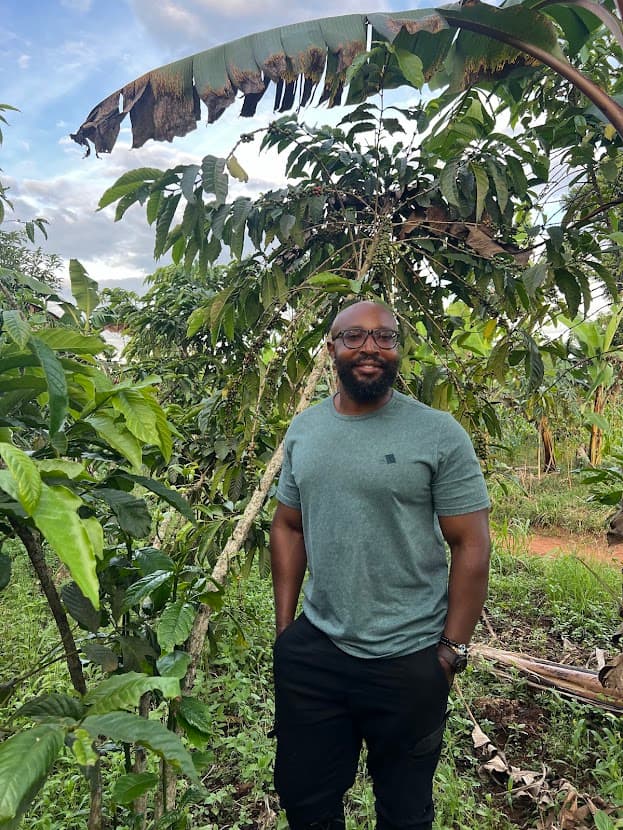 Ben Serunyigo, founder of Nyaliko, standing among coffee trees on a Ugandan farm